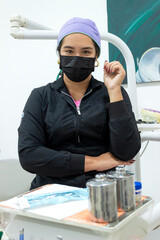 Portrait of a Hispanic female orthodontist sitting in uniform and wearing a mask, looking at the camera inside a dental office in Neiva, Huila, Colombia. Concept of  dentistry and job