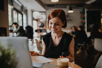 A portrait of woman working remotely from coffee shop, using laptop.