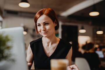 A portrait of woman working remotely from coffee shop, using laptop.