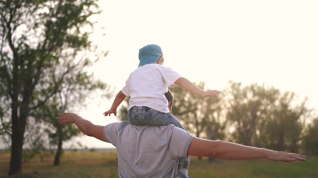 Father and son playing together piggyback in the park. Male care summer concept. Father carrying son to the back. Father and son carries his lifestyle daughter together in the park.