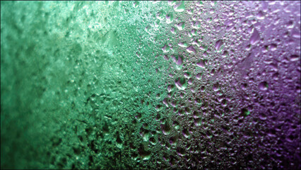 Close-up of vibrant green and purple condensation droplets on a textured surface, showcasing abstract light reflections and water patterns.