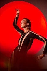 A slender, athletic woman poses in a studio against a red backdrop.
