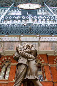London, England - September 10, 2012: Bronze lovers&rsquo; embrace beneath the iconic clock at St Pancras International, framed by Victorian brickwork and the station&rsquo;s striking iron and glass roof structur