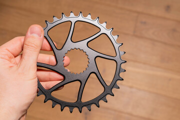 Close-up of a hand holding a black bicycle chainring with spline interface and weight-reducing cutouts