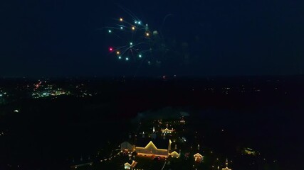 A vibrant fireworks show lights up the night sky above a picturesque town. The colorful bursts create a stunning contrast against the dark backdrop, enchanting viewers from below.