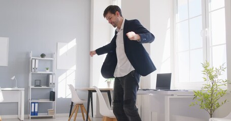 Happy businessman dances merrily in his office celebrating professional achievement. Man in suit rejoicing in triumph demonstrating importance of celebrating successes in professional environment.