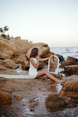 young, slender woman in a white dress walks barefoot on a sandy beach.