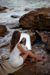 young, slender woman in a white dress walks barefoot on a sandy beach.