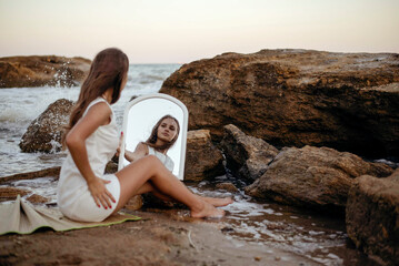 young, slender woman in a white dress walks barefoot on a sandy beach.