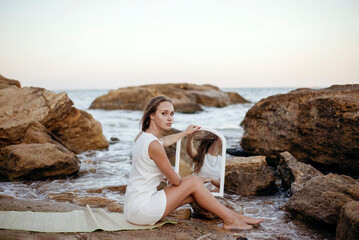 young, slender woman in a white dress walks barefoot on a sandy beach.