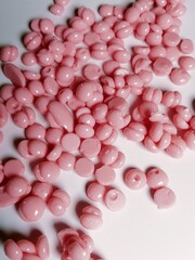 The photo shows pink wax beads shot from a close-up. The surface texture is smooth and shiny, highlighting the small, round shape typical of wax beads. The photo was taken from various angle 