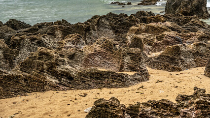 Layered rock formations on a sandy beach with ocean waves in the background. Geological textures shaped by erosion and sedimentation