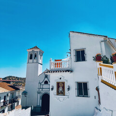Church and house in typical white Spanish Andalucian village under a clear blue sky. Almogia, Malaga, Andalusia, Spain.