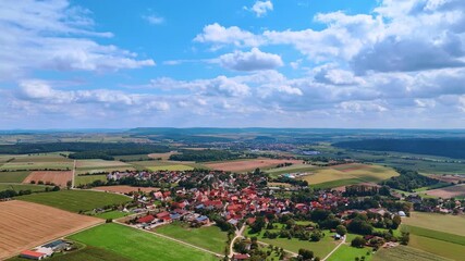 A rural village surrounded by wide multi-colored fields under a cloudy sky. A general view of a small settlement in a picturesque valley among green and plowed lands.