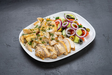 Grilled chicken slices with fresh Greek salad of cucumber, tomato, onion and olives on plate