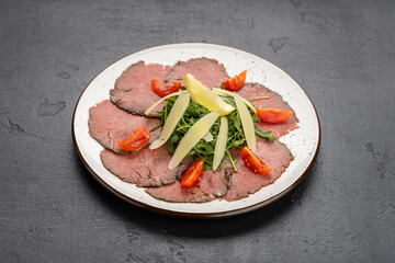 Beef carpaccio with arugula, parmesan shavings and lemon on a plate