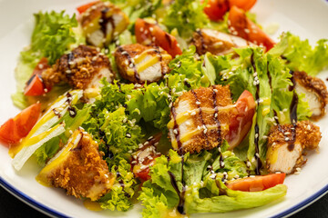 Crispy chicken salad with lettuce, tomatoes, sesame and dressing on plate