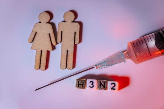 Wooden figures representing male and female, alongside a syringe and letter blocks spelling H3N2, illustrating health concepts and vaccination awareness in a creative composition