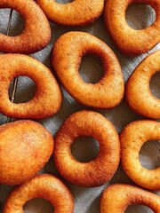 Golden homemade donuts arranged in rows on a baking sheet. Concept of baking, desserts, comfort food, homemade treats, and pastry backgrounds