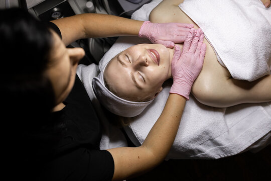 Face and neck massage at a beautician's appointment. Adult Caucasian woman gets treatments, specialist in pink latex gloves