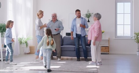 Positive older generation parents and grandparents having conversation, standing in living room with cheerful active children having fun and playing around them. Happy multi generation family concept. - Powered by Adobe