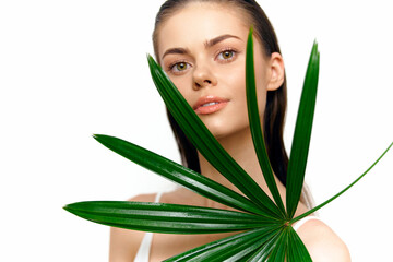 Naklejka premium Young model with a palm leaf, showcasing natural beauty and freshness in a bright, minimalist setting with vibrant greenery.