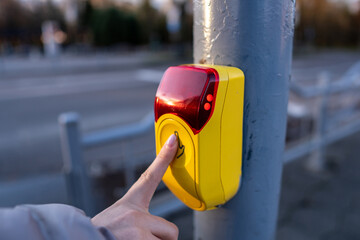 Pedestrian presses crossing button at traffic signal on city street during late afternoon hours