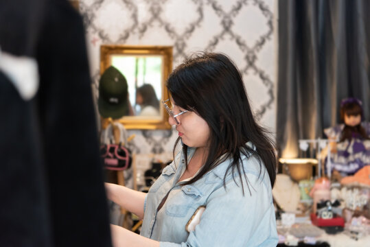 Two LGBTQ friends enjoy shopping for trendy clothes at a fashionable store. One of them is looking at a stylish item, considering it. The store offers a variety of fashionable options and accessories.