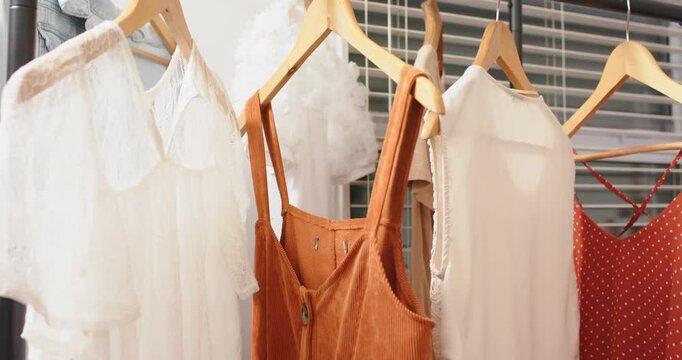 wooden hangers on metal rack swaying clothes against shop blinds, camera panning showing colors