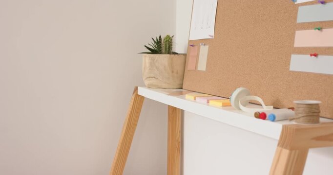 Camera panning right across home office shelf, revealing succulent, corkboard, markers, twine, tape