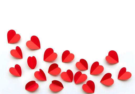Top-down view of folded red paper hearts scattered across the bottom half of a white surface, leaving ample copy space above.