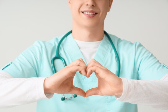Male nurse making heart gesture on light background, closeup