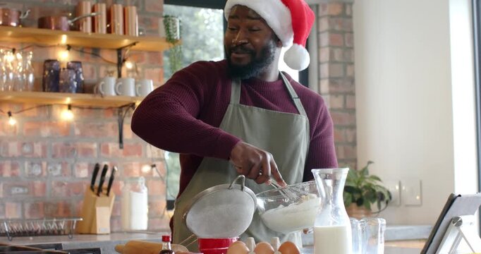 African American man tapping sieve to sift flour, whisking batter for baking in kitchen smiling