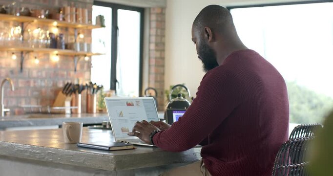 Man is opening laptop lid at kitchen island, scanning charts and typing to analyze data