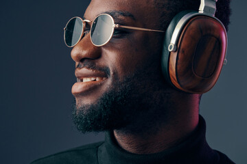 Obraz premium Stylish young man wearing headphones and sunglasses, showcasing a confident expression, with a modern dark background highlighting his trendy look and love for music