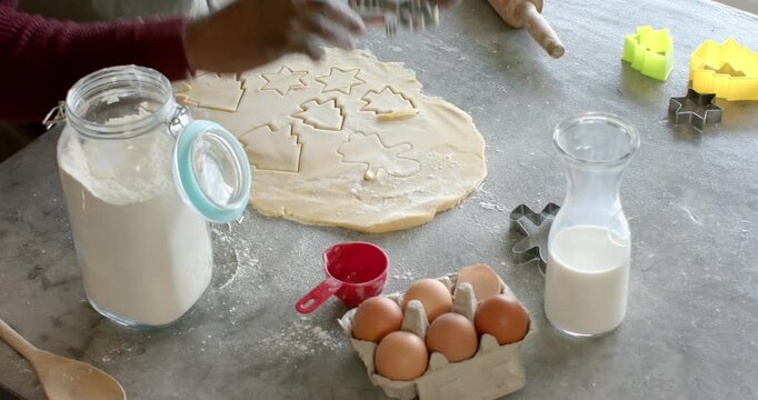 Baker's hands reaching for cutter, stamping star, tree shapes into dough on countertop for baking