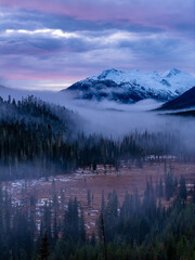 Snowy Mountain Lake Scene With Misty Forest And Purple Sunset In BC, Canada