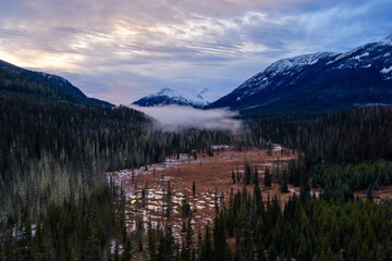 Snowy Mountain Valley With Misty Dawn Over Dense Forests in British Columbia, Canada