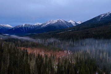 Fototapeta premium Snow-Topped Mountain Range Over Dense Forest With Misty Valley in British Columbia, Canada