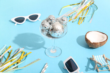 Glass with disco balls, sunglasses and decor on blue background