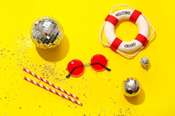 Disco balls with sunglasses, straws and lifebuoy on yellow background