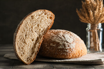 Napkin with cut loaf of fresh bread and wheat on grey tiled table