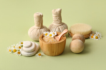 Massage herbal bags, chamomile flowers and bowl with sea salt on green background, closeup