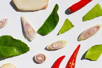 A colorful, close-up pattern of Thai herbs: lime slices, galangal, lemongrass, chilies, and kaffir lime leaves.