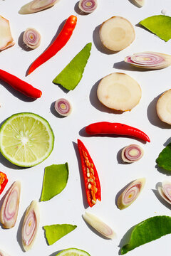 A colorful, close-up pattern of Thai herbs: lime slices, galangal, lemongrass, chilies, and kaffir lime leaves.