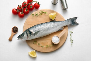 Wooden board with fresh raw seabass fish and different ingredients on white background