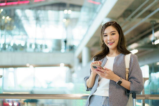 Asian woman using smartphone while waiting inside a modern airport.
