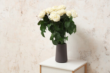 Bouquet of beautiful white roses in vase on table against light background