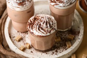 Glasses of cocoa drink with whipped cream and sugar cubes on brown background