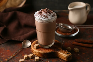Glass of cocoa drink with whipped cream, cinnamon sticks and sugar cubes on grunge background